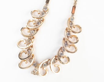 Può includere: Una collana d'oro con un design delicato che presenta una serie di forme di cuore collegate adornate con strass trasparenti.