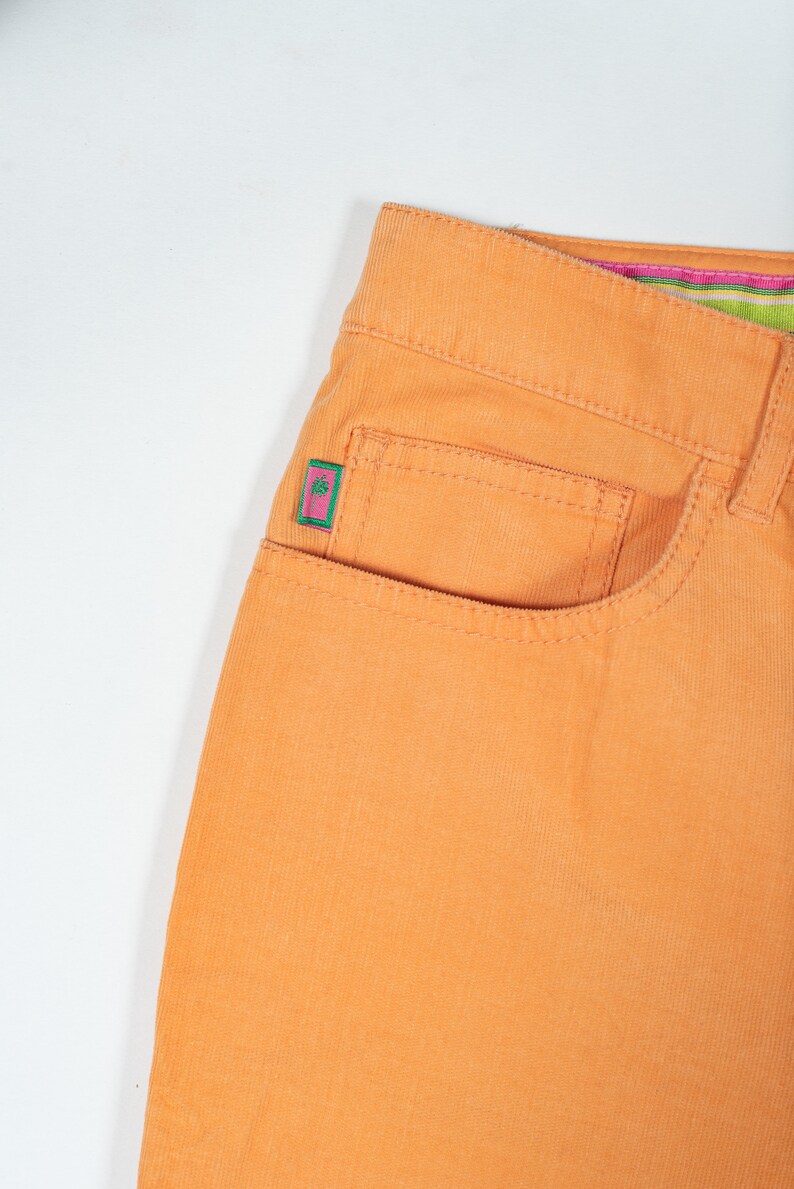 May include: Orange corduroy pants with a small pink and green patch on the front pocket.