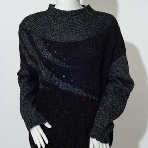 Può includere: Un maglione di lana nero e grigio con collo alto e un sottile motivo di paillettes argentate. Il maglione ha una vestibilità rilassata e un orlo a coste.