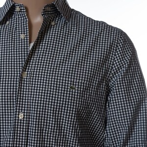 May include: A button-down shirt with a navy and white checkered pattern. The shirt has a small pocket on the chest and a green crocodile logo. The collar is buttoned down, and the shirt is partially unbuttoned.