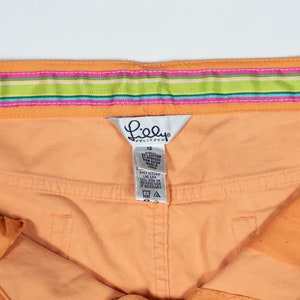 May include: Orange shorts with a pink, green, and blue striped waistband. The shorts have a Lilly Pulitzer tag with the size 12 printed on it.