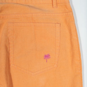 May include: Orange corduroy pants with a back pocket featuring a pink palm tree embroidery.