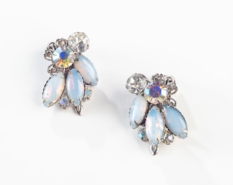Può includere: Un paio di orecchini in argento con strass blu iridescenti e trasparenti. Gli orecchini hanno un gruppo di pietre in un design a forma di fiore.