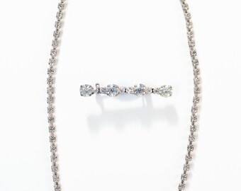 Può includere: Una collana d'argento con una fila di strass trasparenti. La collana ha una chiusura a moschettone e un ciondolo abbinato con una fila di strass trasparenti.
