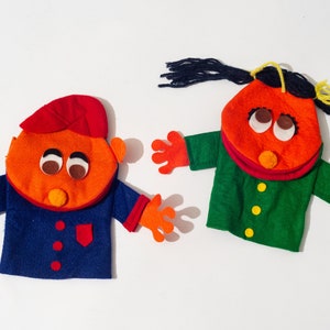 May include: Two felt hand puppets, one with a red hat and blue jacket, the other with a green jacket and black yarn hair.