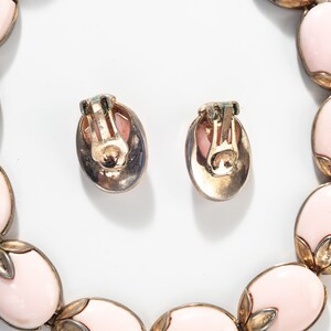 Puede incluir: Un conjunto de pendientes ovalados de color rosa y un collar a juego. Las joyas est&aacute;n hechas de metal dorado y presentan un delicado dise&ntilde;o floral.