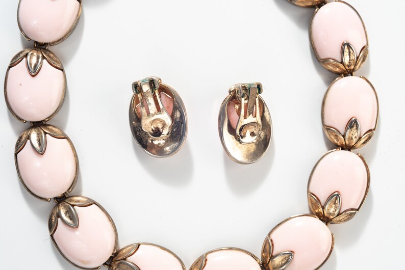Puede incluir: Un conjunto de pendientes ovalados de color rosa y un collar a juego. Las joyas est&aacute;n hechas de metal dorado y presentan un delicado dise&ntilde;o floral.