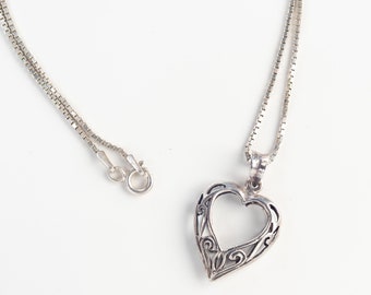 Può includere: Una collana d'argento con una catena delicata e un ciondolo a forma di cuore traforato.