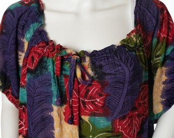 Può includere: Una blusa ampia e colorata con un nodo sul collo e una chiusura con bottoni sul davanti. Il tessuto presenta una stampa floreale astratta vibrante in tonalità di rosso, viola, verde e giallo.