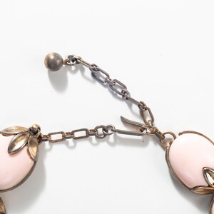 Puede incluir: Un collar rosa y dorado con piedras de forma ovalada y una cadena delicada. El collar tiene un cierre de metal.