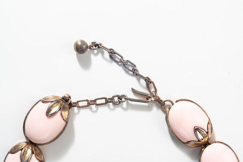 Puede incluir: Un collar rosa y dorado con piedras de forma ovalada y una cadena delicada. El collar tiene un cierre de metal.