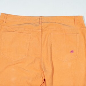 May include: A pair of orange cotton pants with two back pockets and a small pink palm tree embroidered on the right back pocket.