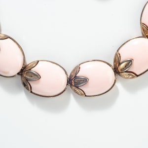 Puede incluir: Un collar rosa y dorado con piedras de forma ovalada y detalles florales.