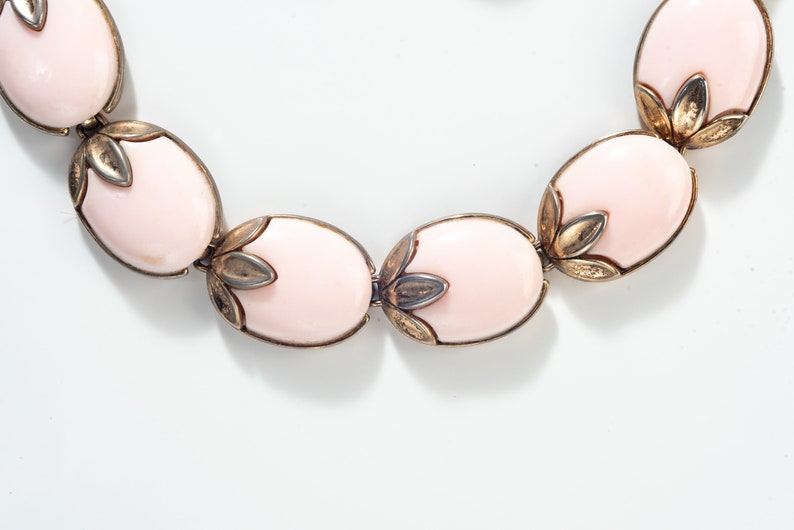 Puede incluir: Un collar rosa y dorado con piedras de forma ovalada y detalles florales.