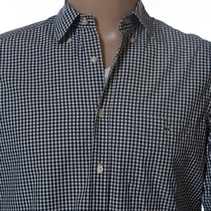 May include: A button-down shirt with a navy and white gingham pattern. The shirt has a chest pocket and a small green logo. The collar is buttoned down. The shirt is on a mannequin.