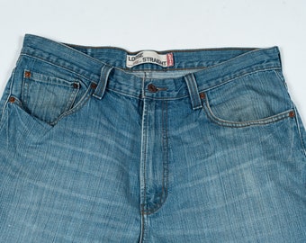 Può includere: Un paio di jeans blu in denim con vestibilità dritta e ampia. I jeans hanno una toppa in pelle marrone con il testo "Loose Straight" sul retro della cintura.