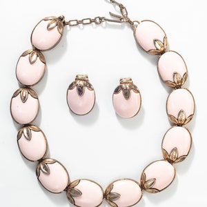 Puede incluir: Un conjunto de collar y pendientes de color rosa y dorado. El collar est&aacute; hecho de piedras rosas ovaladas con detalles dorados. Los pendientes tambi&eacute;n son ovalados y tienen un dise&ntilde;o similar.