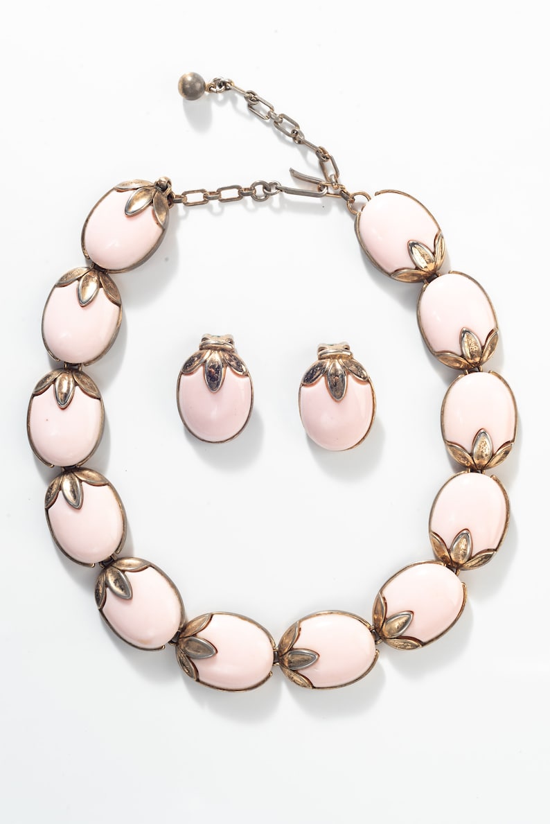 Puede incluir: Un conjunto de collar y pendientes de color rosa y dorado. El collar est&aacute; hecho de piedras rosas ovaladas con detalles dorados. Los pendientes tambi&eacute;n son ovalados y tienen un dise&ntilde;o similar.