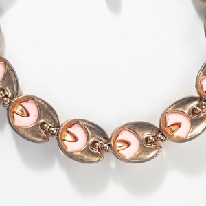 Puede incluir: Un brazalete de tono dorado con acentos de esmalte rosa. El brazalete est&aacute; hecho de eslabones ovalados con un dise&ntilde;o decorativo.