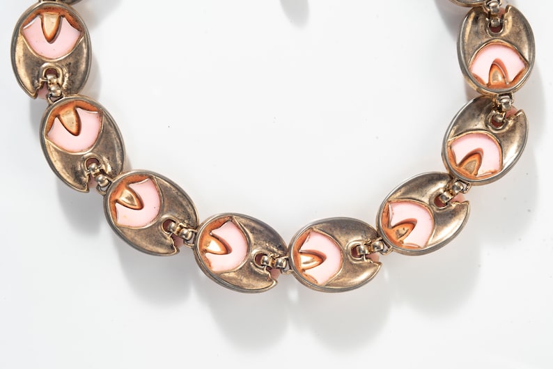 Puede incluir: Un brazalete de tono dorado con acentos de esmalte rosa. El brazalete est&aacute; hecho de eslabones ovalados con un dise&ntilde;o decorativo.
