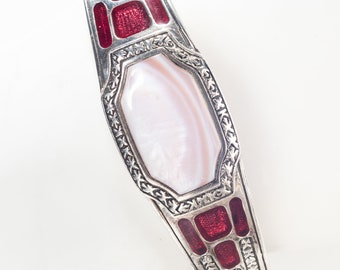 Può includere: Un braccialetto d'argento con un designo in smalto rosso e bianco. Il braccialetto presenta un'ampia intarsio ovale in madreperla.