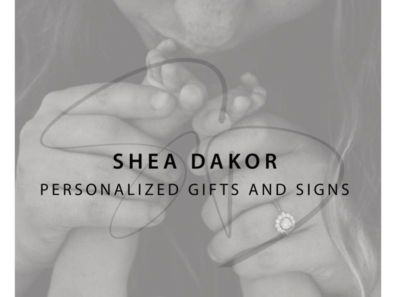 May include: Monochrome image featuring the text "SHEA DAKOR PERSONALIZED GIFTS AND SIGNS." The image shows hands holding a baby's foot and a ring with a floral design.
