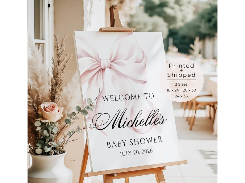 May include: A baby shower welcome sign on an easel. The sign features a large pink bow illustration and the words "Welcome to Michelle's Baby Shower July 20, 2026". The sign is available in 3 sizes: 18 x 24, 20 x 30, and 24 x 36 inches.