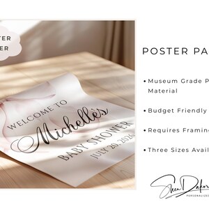 May include: A rolled poster on a wooden surface, featuring the text "Welcome to Michelle's Baby Shower July 20, 2026." The poster has a soft pink floral design. The words "Poster Paper" are in a cloud-shaped text box.