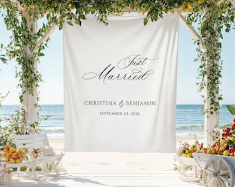 May include: A white banner with the words "Just Married" in elegant script, along with the names Christina & Benjamin and the date September 22, 2026. The banner hangs on a white wooden structure decorated with greenery, set against a beach backdrop.