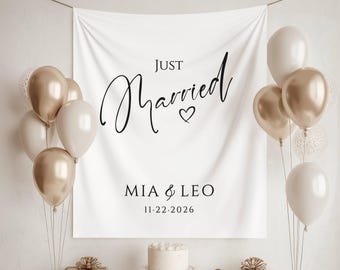 May include: A white backdrop with the words "Just Married" in elegant black script, accompanied by a heart symbol. Below, the names "MIA & LEO" and the date "11.22.2026" are displayed. Balloons in gold, white, and clear with confetti accents frame the backdrop.