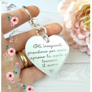 Puede incluir: Un llavero de corazón plateado con la inscripción "Gli insegnanti prendono per mano, aprono la mente e toccano il cuore" y el texto "Costa Creations" en la parte inferior.