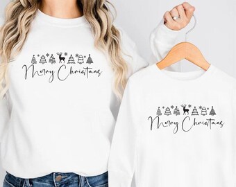 Puede incluir: Dos sudaderas blancas, una puesta y otra en una percha, ambas con un gráfico negro con temática navideña. El gráfico incluye árboles, copos de nieve, un reno y el texto cursivo "Merry Christmas".
