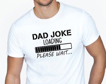 May include: White t-shirt with the text "DAD JOKE LOADING PLEASE WAIT..." in black. The design includes a loading bar graphic. The shirt is short-sleeved and appears to be made of cotton.