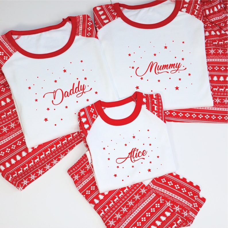 May include: Matching family Christmas pajamas. White tops with red trim and the names "Daddy", "Mummy", and "Alice" in red script. Red bottoms with a white reindeer and snowflake pattern. A festive holiday ensemble.