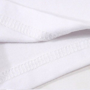 May include: Close-up of white fabric with visible stitching. The fabric appears to be a soft material, possibly cotton or a blend, with a clean, crisp appearance. The stitching is a contrasting white thread.