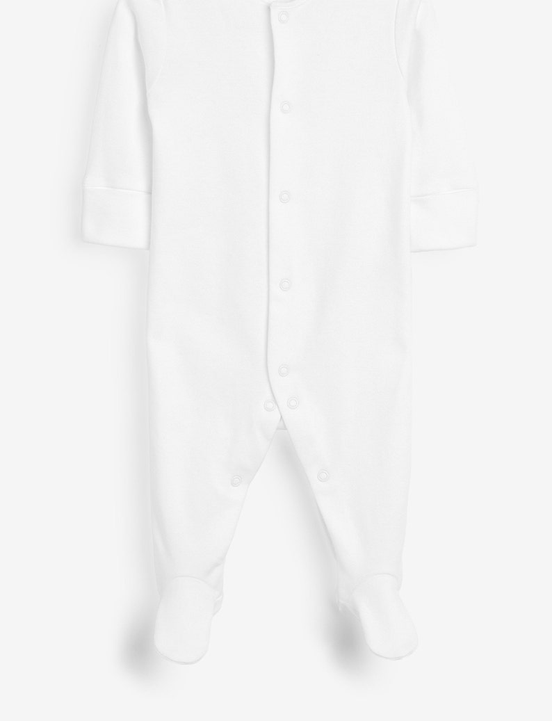May include: A white baby sleeper with long sleeves and attached feet. The sleeper has a button-up front closure and is made of a soft, comfortable fabric. The cuffs on the sleeves are folded over.