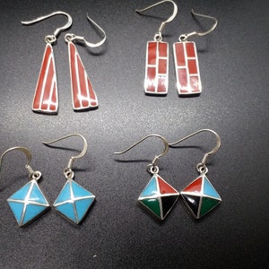 May include: Four pairs of dangle earrings with geometric designs. The earrings are made of silver and have colourful enamel accents. The designs include a red and white triangle, a red and white rectangle, a blue diamond, and a green, black and red diamond.