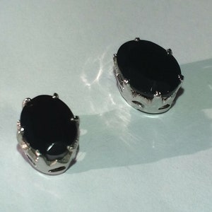 May include: A pair of silver earrings with black oval-shaped gemstones set in a crown-like design.