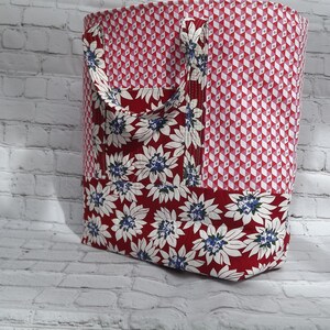 Può includere: Una borsa tote rossa e bianca con un motivo floreale. La borsa ha due manici ed è realizzata in tessuto.