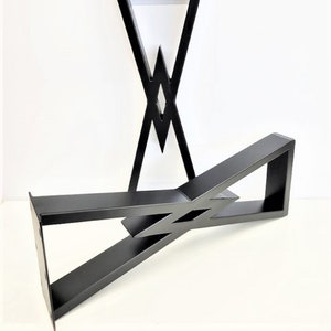 May include: Black metal table legs with a geometric design. The legs feature a diamond-shaped cutout and angled supports, creating a modern aesthetic. The legs are designed for a table or desk.