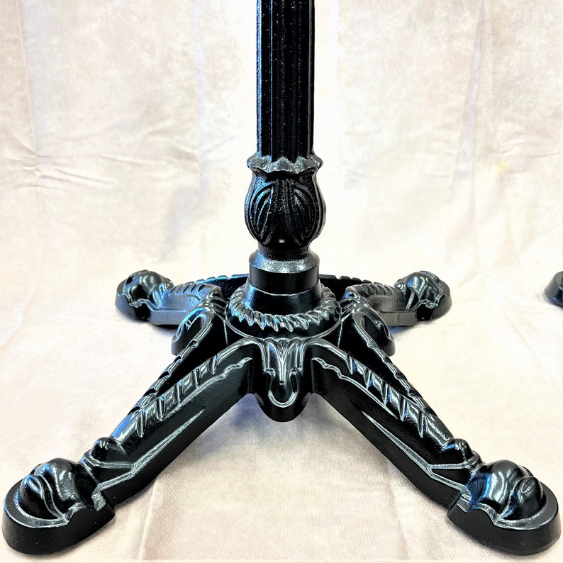 Pu&ograve; includere: Base per tavolo in metallo nero con un design a tre gambe. Ogni gamba presenta dettagli intricati e un piede arrotondato.
