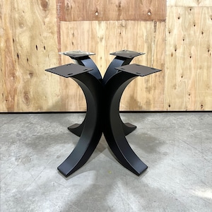 May include: Black metal table base with four curved legs and square mounting plates. The base is designed to support a tabletop and has a modern, minimalist aesthetic. The base is made of metal and is painted black.