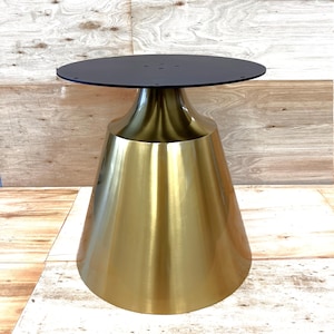 May include: A modern side table with a black circular top and a gold-colored, flared base. The table has a sleek, metallic finish and a contemporary design, suitable for various interior styles.