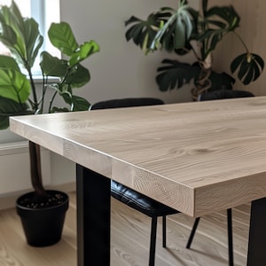 May include: A light wood dining table with a natural finish and black metal legs. The table is shown with two black chairs.