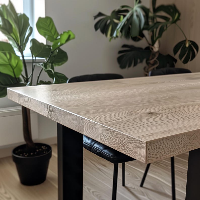 May include: A light wood dining table with a natural finish and black metal legs. The table is shown with two black chairs.