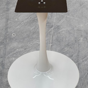 May include: A white tulip-style table base with a round base and a square top. The stem is a light beige color. The top is a dark brown metal plate with screw holes.