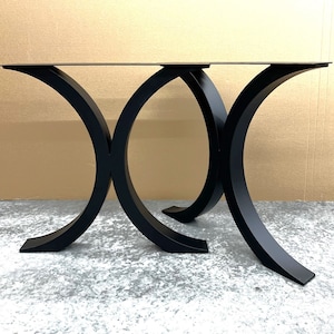 May include: Two black metal table legs with a curved, X-shaped design. The legs are made of thick, sturdy metal and have a sleek, modern look.