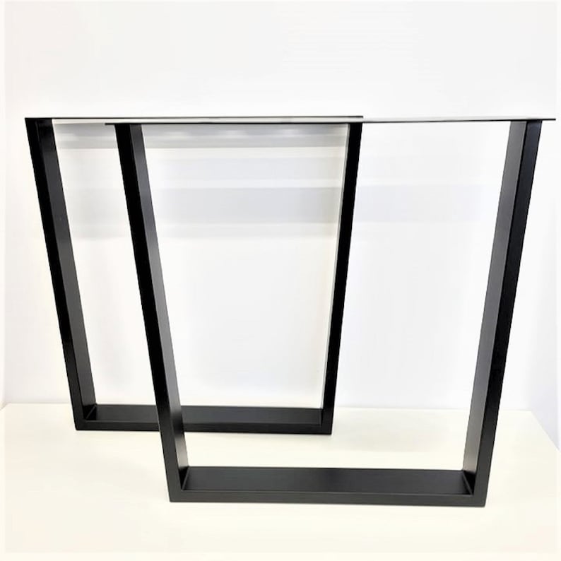 May include: Two black metal table legs with a trapezoidal shape. The legs are made of sturdy metal and have a black powder-coated finish.
