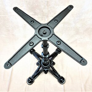 Pu&ograve; includere: Base per tavolo in metallo nero con un design a quattro punte e una colonna centrale. La base ha una finitura testurizzata e un design a forma di stella nella parte inferiore.