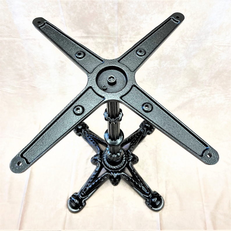 Pu&ograve; includere: Base per tavolo in metallo nero con un design a quattro punte e una colonna centrale. La base ha una finitura testurizzata e un design a forma di stella nella parte inferiore.